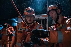 It is a dark and rainy night. Two VICSES volunteers dressed in orange and safety harnesses are undertaking Safe Working from Heights training.